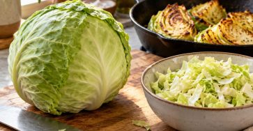 A fresh green cabbage, safely resting chef knife, chopped cabbage in a bowl and golden roasted cabbage wedges in a skillet on a home kitchen counter